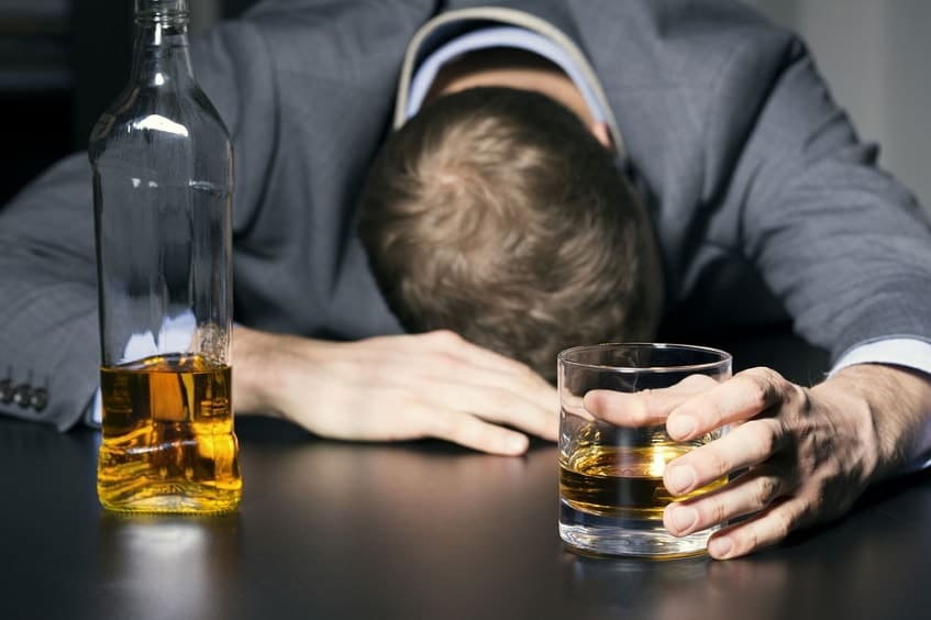 мужчина спит за столом, сжимая в руке стакан с алкоголем